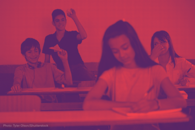Boys in a classroom throwing paper airplanes at a female student sitting in front of them