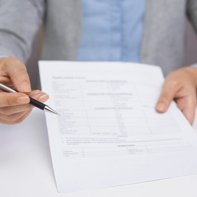 Image of a hand offering a pen to sign a document