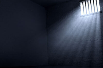 Light streaming through a barred window casts a shadow of the bars the floor of a prison cell