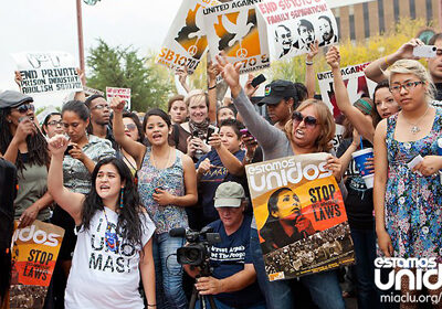 A group of protestors wearing shirts and holding signs that read "Estamos Unidos" and "Stop the Laws"