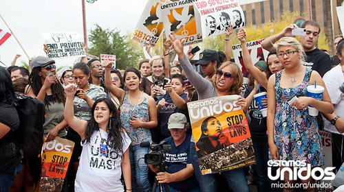A group of protestors wearing shirts and holding signs that read "Estamos Unidos" and "Stop the Laws"