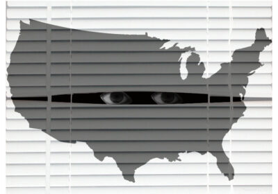 A pair of eyes looks through a break of venetian blinds while an transparent grey image of the US is in the foreground.