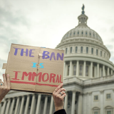 Person holding "The Ban Is Immoral" sign in front of Capitol building
