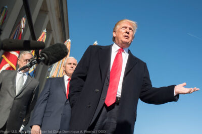 President Trump with his hand extended in front of a microphone