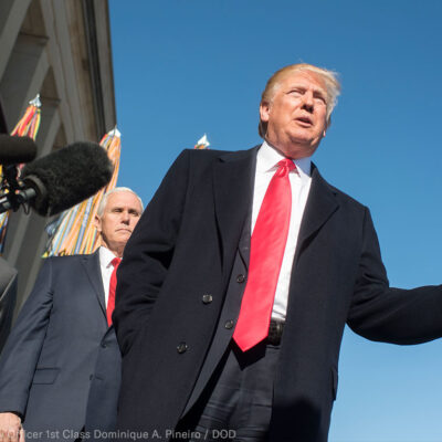 President Trump with his hand extended in front of a microphone