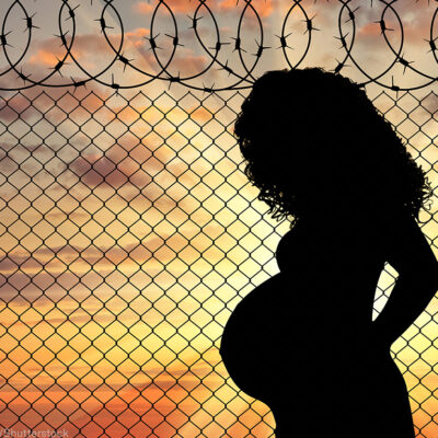 Silhouette of a pregnant woman standing near a fence with barbed wire