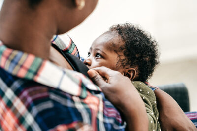 A Black person chest-feeding an infant
