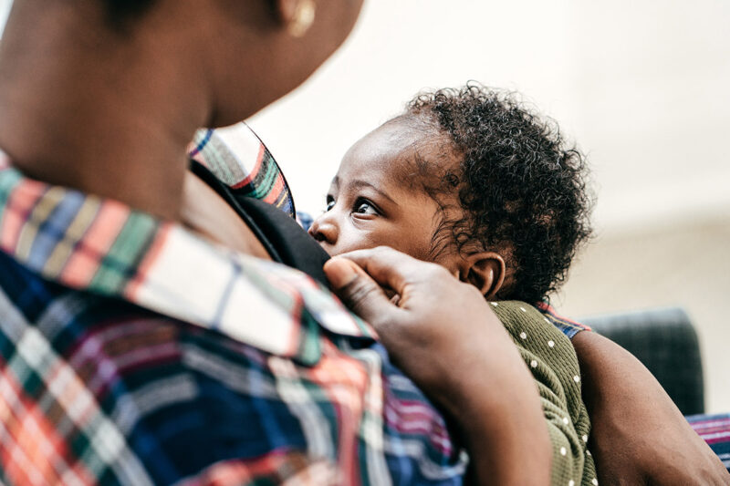 A Black person chest-feeding an infant