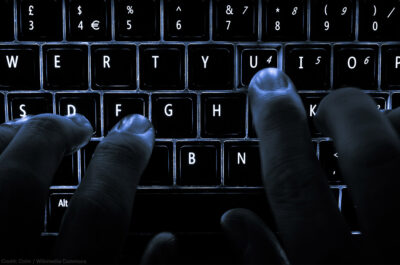 A backlit laptop computer keyboard. Most fingers are on the "home" keys for touch-typing; the 'U' key is being pressed.