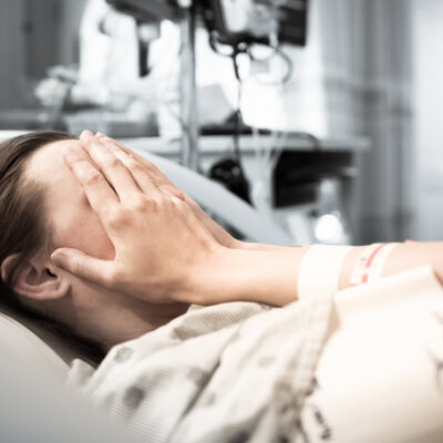 Image of a woman in a hospital bed covering her eyes