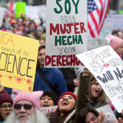 A crowd of people at a protest hold signs in english and spanish