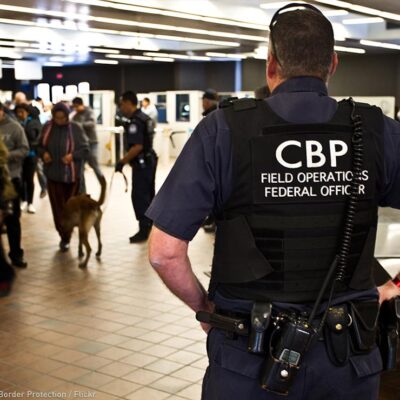 A CBP officer watches over travellers at an airport.