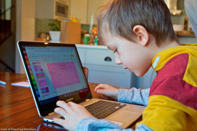 A young child works at home remotely on an online class assignment.