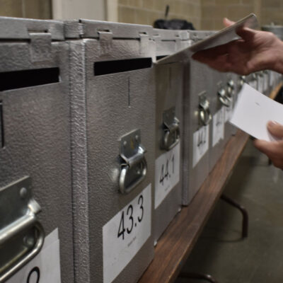 An election worker inserting a ballot into a locked ballot box.