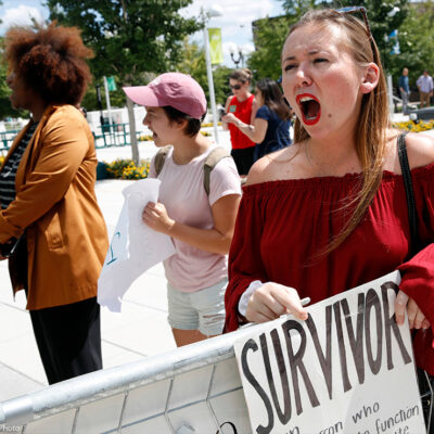 A recent graduate shouts and holds sign that reads "survivor" as Betsey Devos speaks on college campus about changes to Title IX