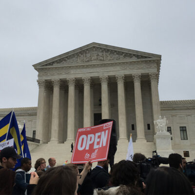Demonstrators outside the Supreme Court with signs advocating for the rights of LGBT people, including a sign with the text "Open to All" in the center.