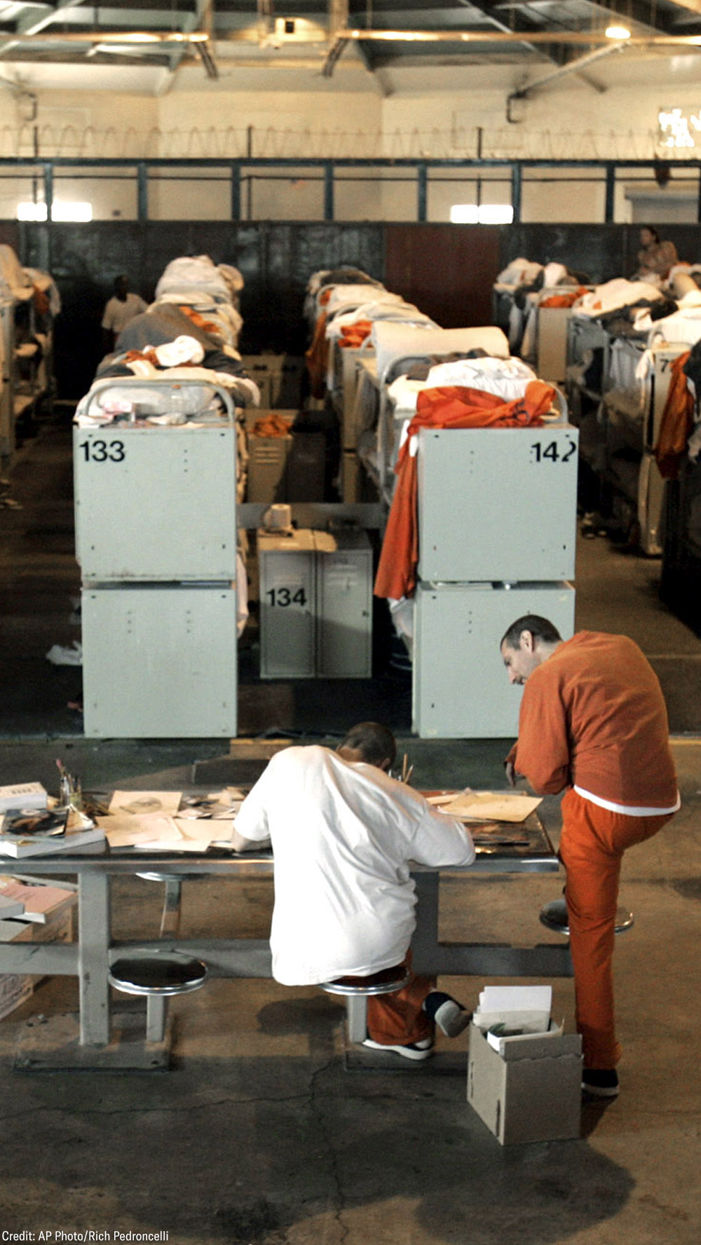 Incarcerated people lying in rows of prison bunk beds.