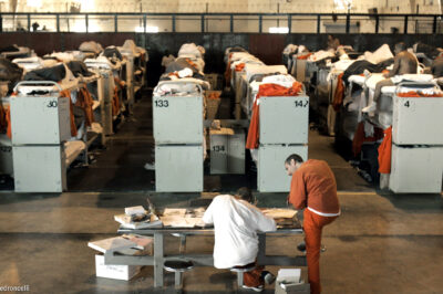 Incarcerated people lying in rows of prison bunk beds.