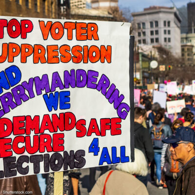 A demonstrator carries a sign demanding an end to gerrymandering and voter suppression.