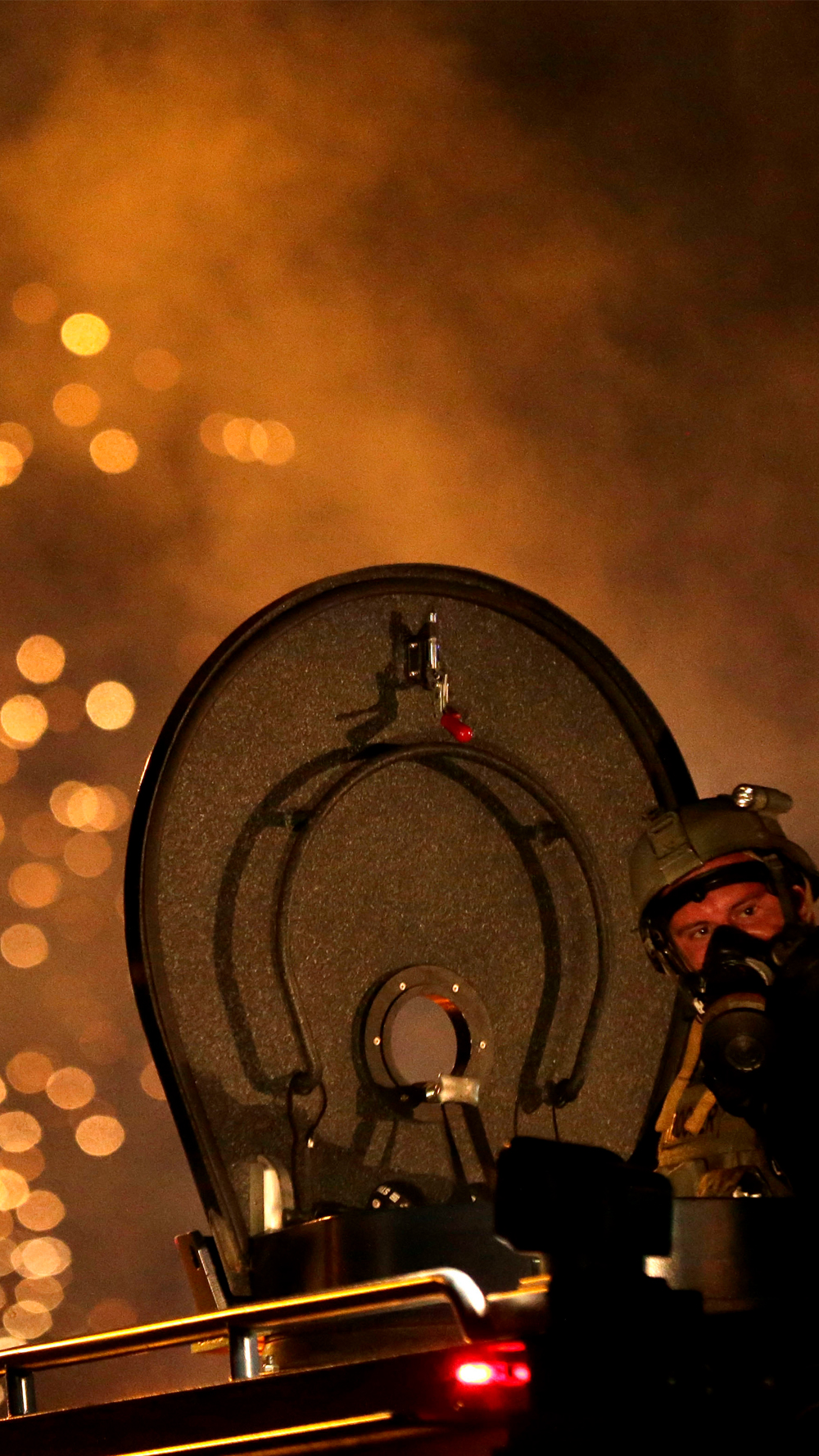 A law enforcement officer watches from an armored vehicle after a device was fired to disperse a crowd during a protest.