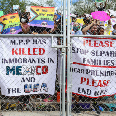 People press signs against a closed gate to the migrant encampment, asking then President Donald Trump to end the Migrant Protection Protocols during a rally at the encampment in Matamoros, Tamaulipas, Mexico on October 25, 2020.