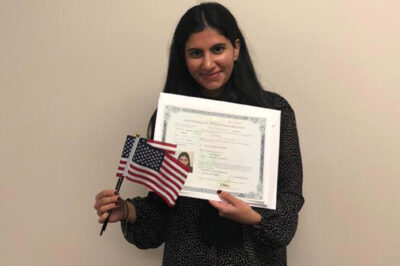 Mira Naseer, a diversity visa recipient, holding her naturalization papers and two American flags.