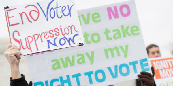 Demonstrators hold signs, one of which says “End Voter Suppression Now.”