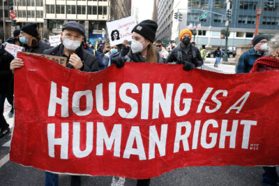Protesters marching and holding a sign reading Housing Is A Human Right.