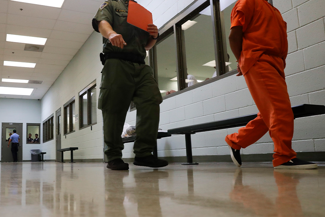A prison guard walks a detainee with his hands behind his back to an intake area at an ICE Processing Center.