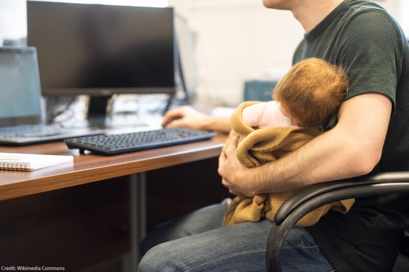 A man holding a baby while on a computer.