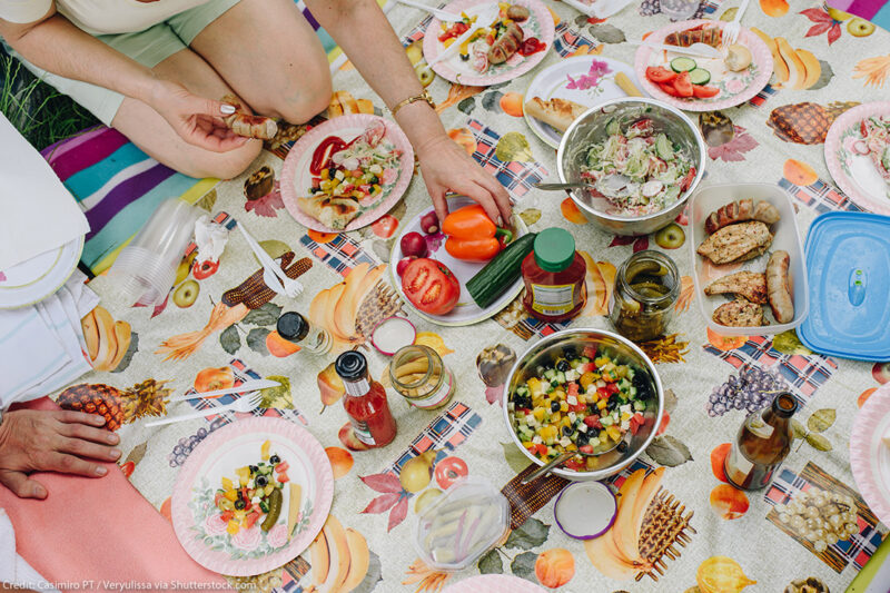 The top view of a picnic outside, with people eating various prepared foods.