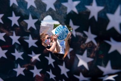 Abortion rights activists are seen through a hole in an American flag as they protest outside the Supreme Court in Washington, Saturday, June 25, 2022.