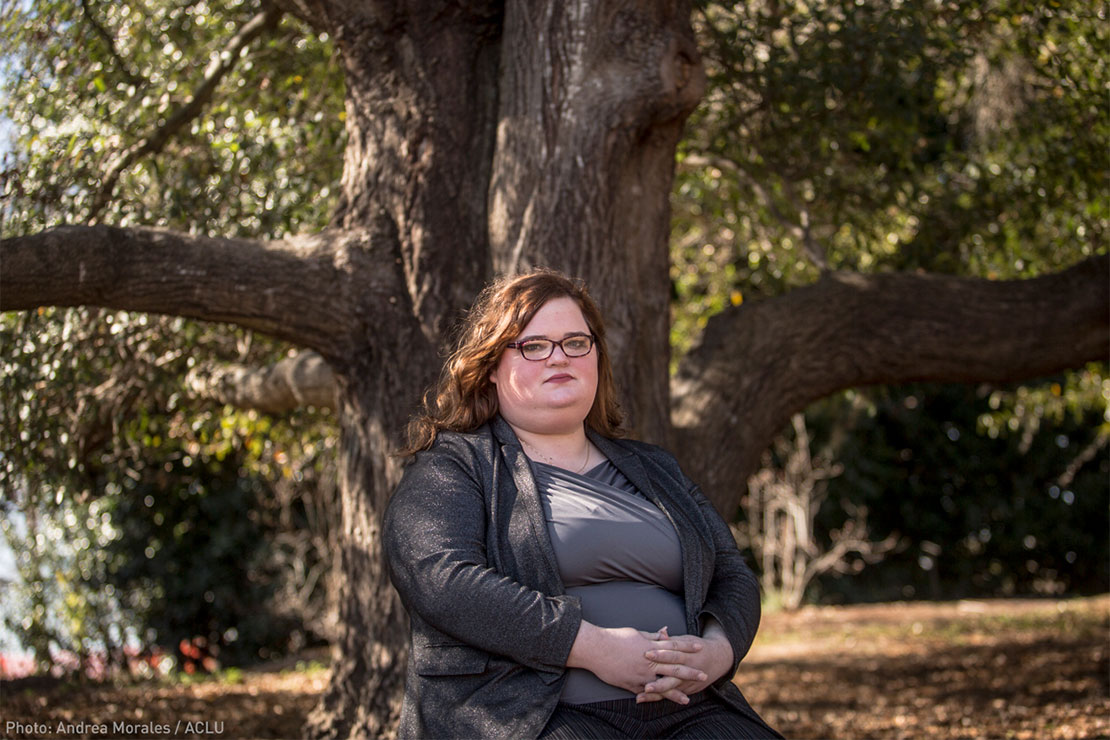 Darcy Corbitt sitting in front a massive tree, looking forward and with fingers interlaced in front of her.
