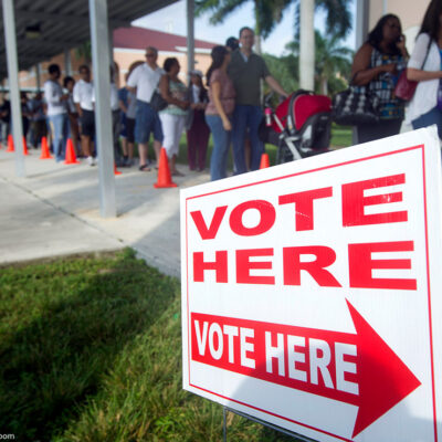 A line of voters in front of a sign that says "vote here."