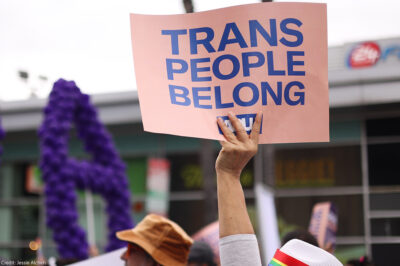 Someone holding a sign saying "Trans People Belong."