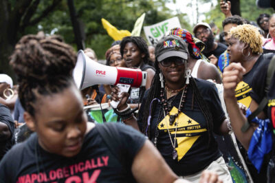 A group of Black marchers holding signs and a megaphone.