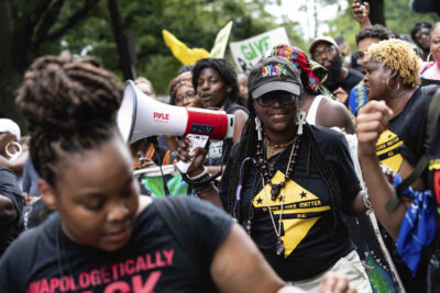 A group of Black marchers holding signs and a megaphone.