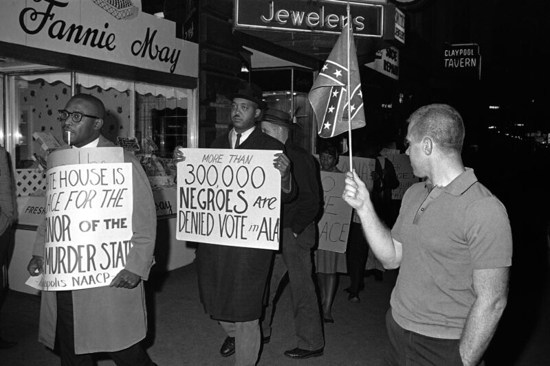 Demonstrators march past a man holding a Confederate flag.