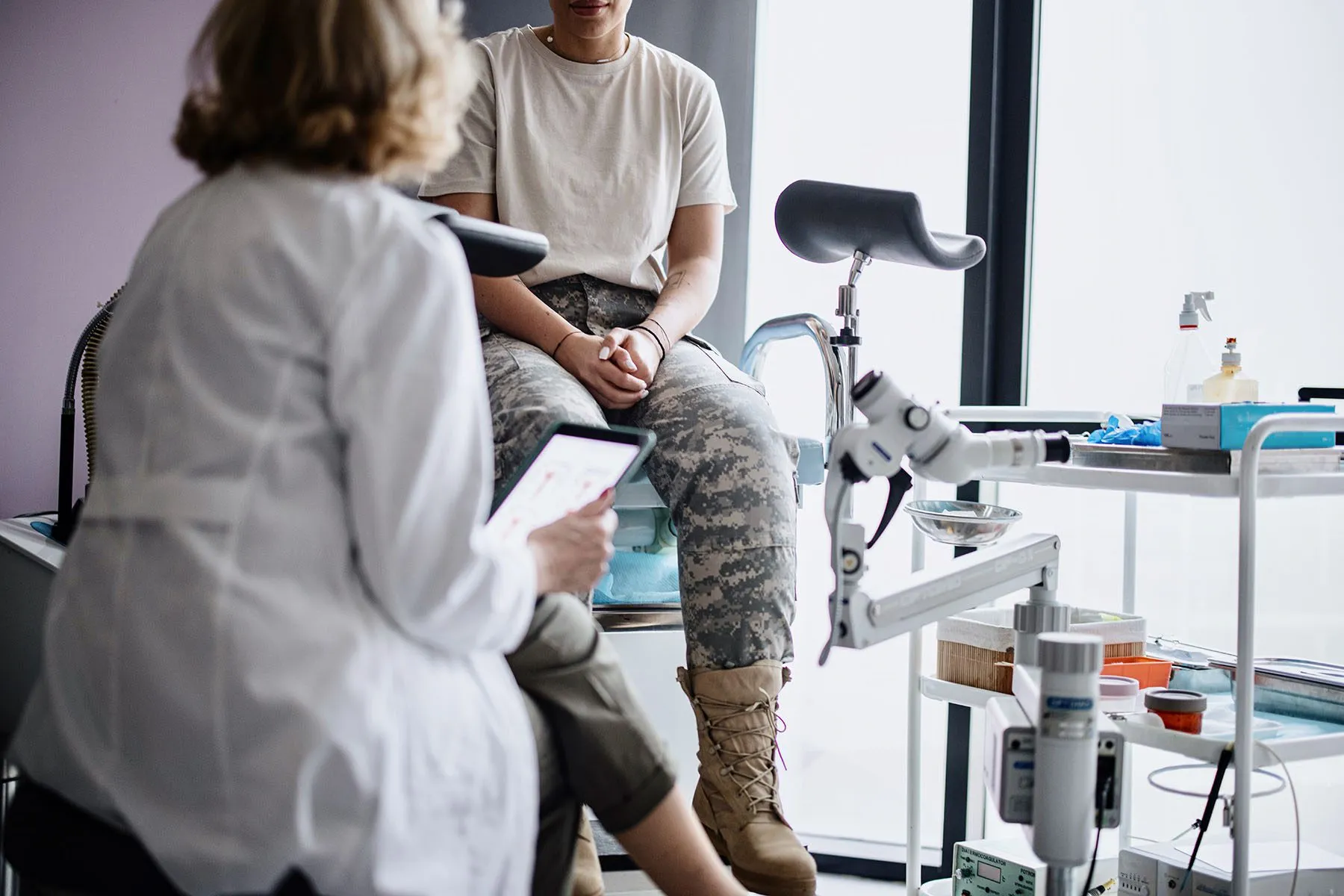 Active duty service member sitting on an examination chair in a doctor's office in front of a physician wearing a white coat