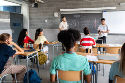 A student presenting in front of a diverse classroom.