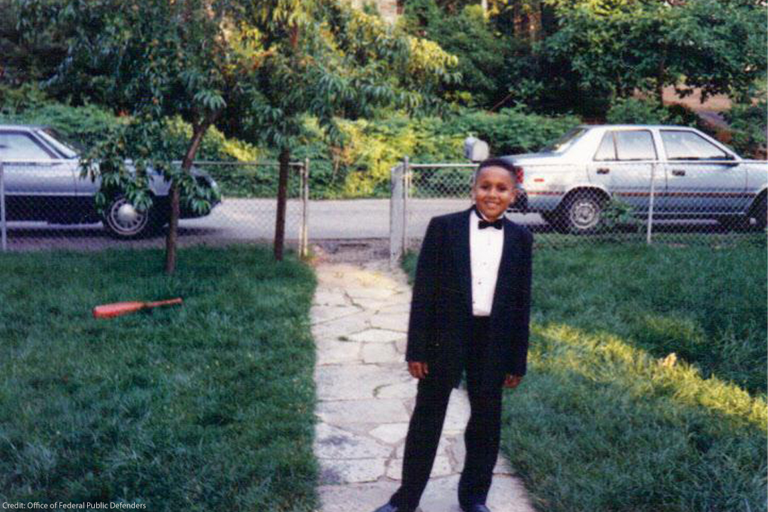 Mikal Mahdi as a middleschooler posing in a tuxedo on a white path on the lawn of his home.