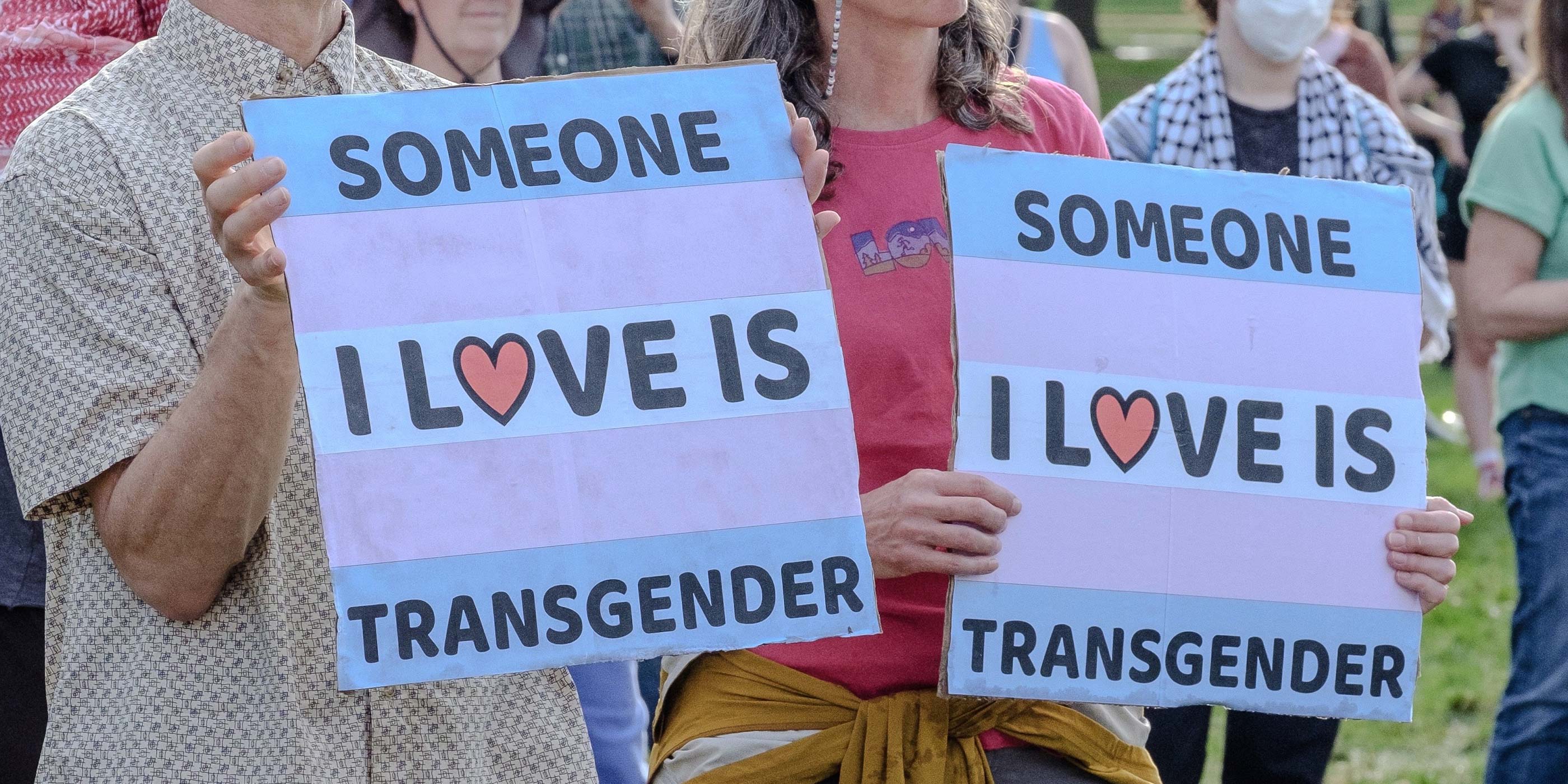 Two people hold up signs that read "SOMEONE I LOVE IS TRANSGENDER".
