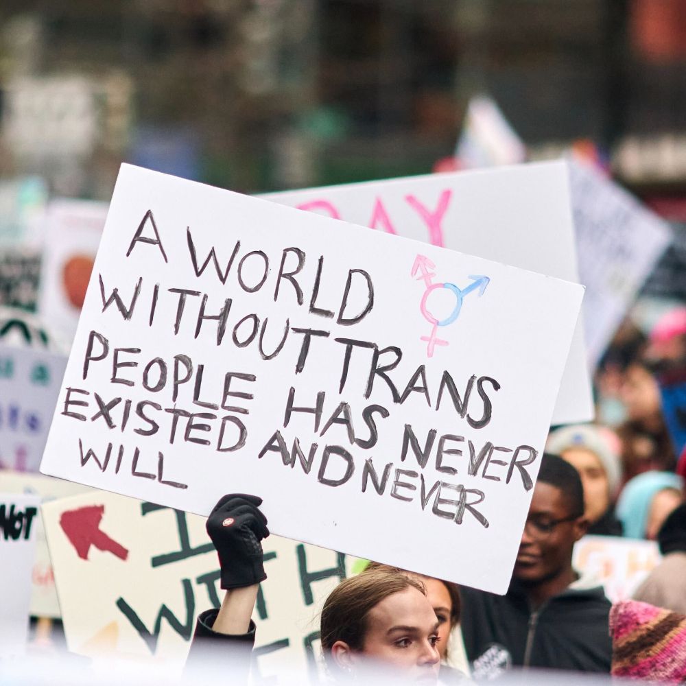 A protestor holds up a sign that says "A world without trans people has never existed and never will.