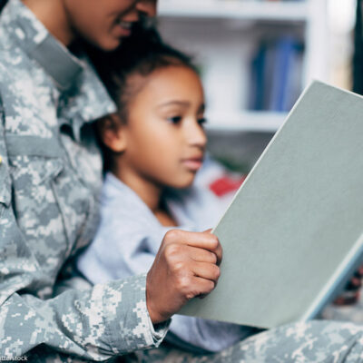 A mother in a military uniform reading to her daughter.