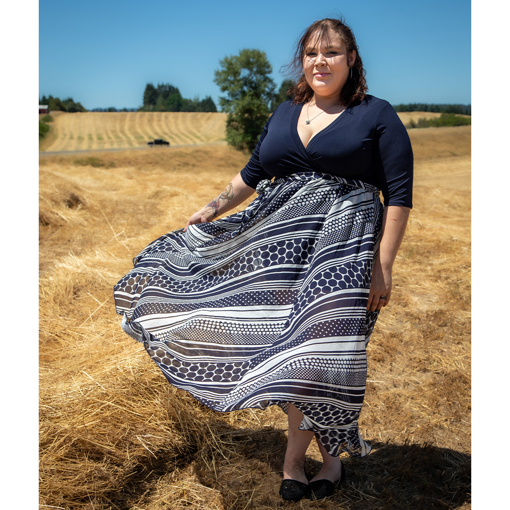 Desiree Guerra whose dress is blowing in the wind, stands in a field of short brown grass.