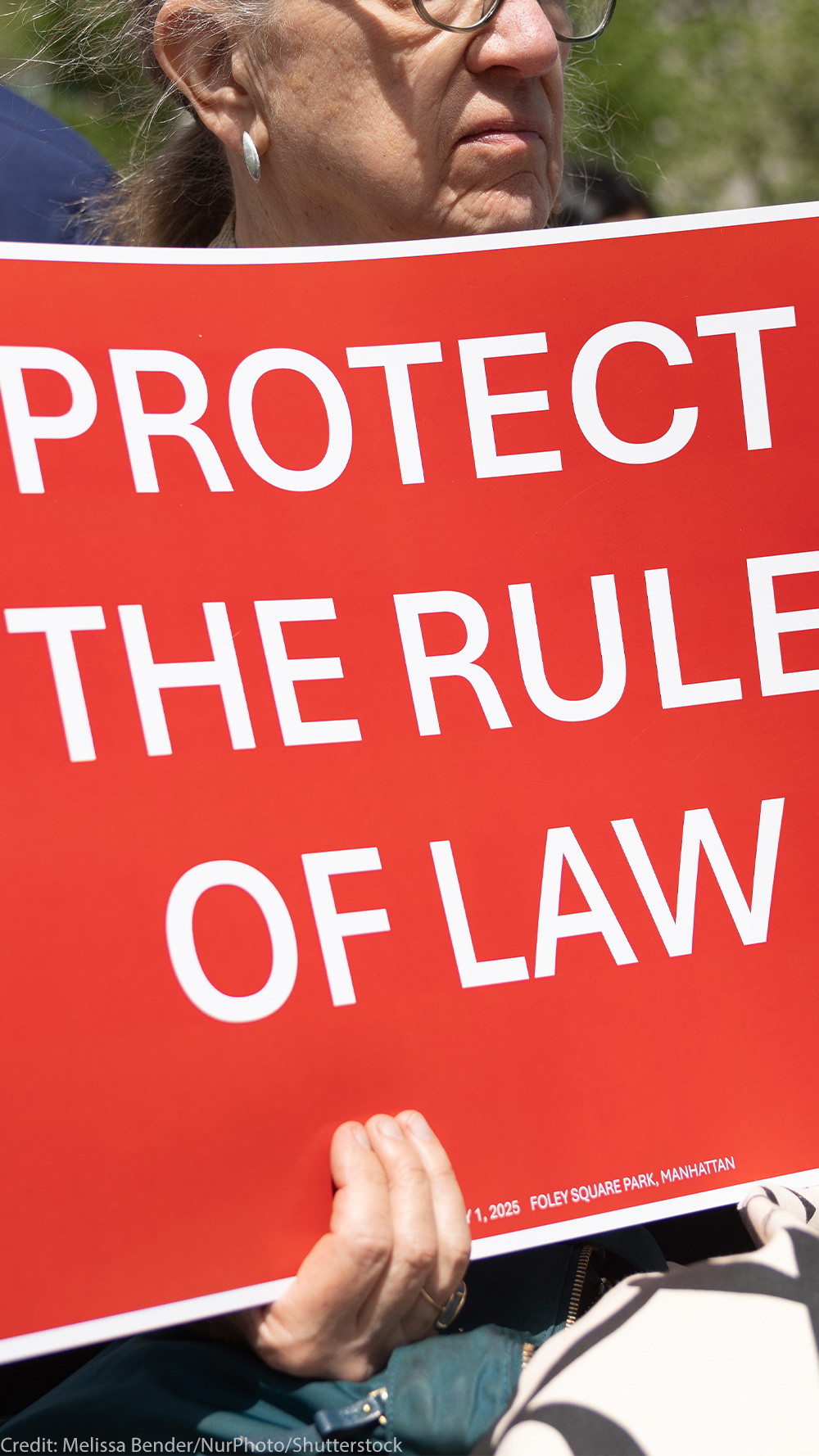 At the Lawyers Rally In Lower Manhattan To Demand Respect For The Rule Of Law, a demonstrator holds up a sign with white lettering on a red background that reds, "PROTECT THE RULE OF LAW".
