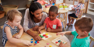 Teacher and pre-K students using wooden shapes.