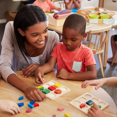Teacher and pre-K students using wooden shapes.