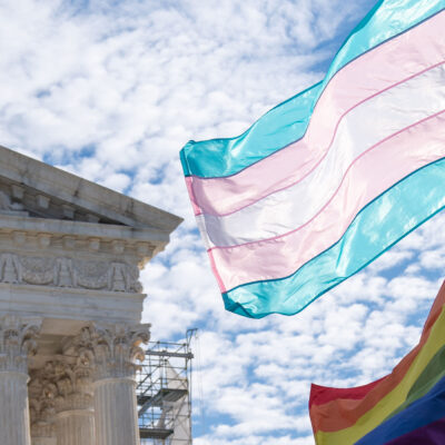 The Trans and LGBTQ+ flags waving in the wind in front of the Supreme Court Building in DC.
