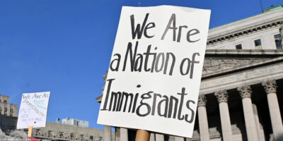 Two signs are held up during the May Day March In Manhattan, New York on May 1, 2025. The largest of the signs is in the foreground and reads"We Are a Nation of Immigrants," while the smaller in the background reads, " WE ARE ALL (EXCEPT NATIVE AMERICANS) IMMIGRANTS! PUT I.C.E. ON ICE NOW".